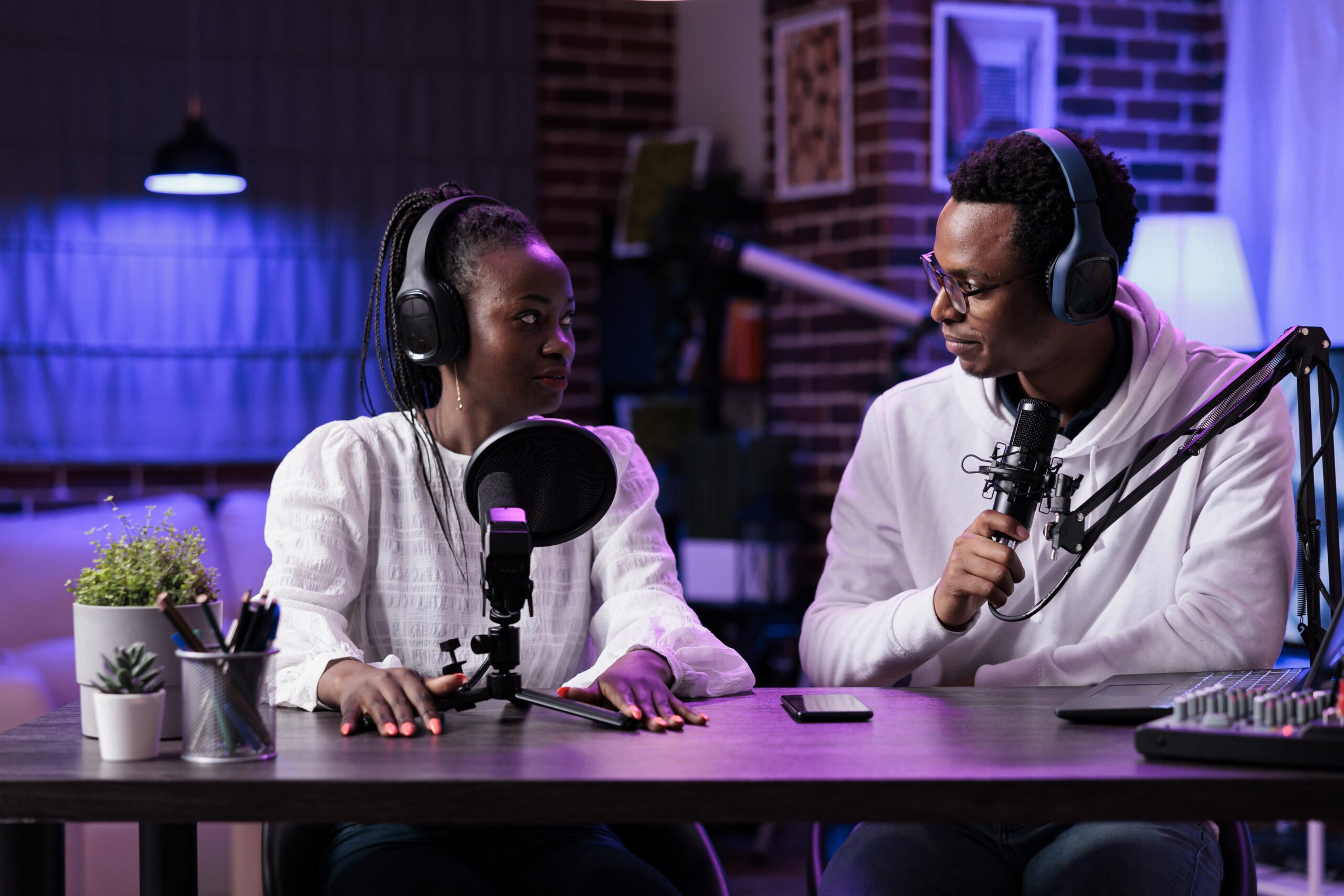 POV of man and woman recording live discussion on camera, doing podcast episode together. Lifestyle influencer talking to female guest in studio with rpg neon lights and equipment.